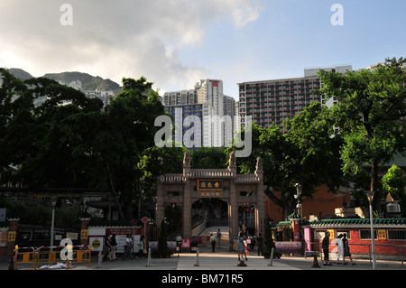 Memorial archway, chinois avec des sculptures sur pierre, l'or nom de temple, des arbres verts et les fidèles, le Temple de Wong Tai Sin,Hong Kong Banque D'Images