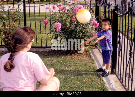 Young Hispanic boy jouer attraper avec ma mère dans la cour avant clôture rose ball fun rire sourire parent famille amour Banque D'Images