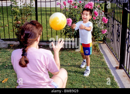 Young Hispanic boy jouer attraper avec ma mère dans la cour avant clôture rose ball fun rire sourire parent famille amour Banque D'Images