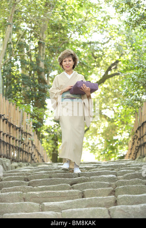 Femme mature en kimono holding gift, descendant des escaliers, la ville de Kyoto, Kyoto Prefecture, Japan Banque D'Images