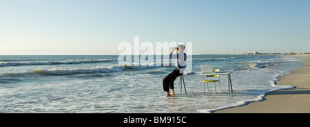 Businessman sitting on desk à la plage, regardant à travers des jumelles en mer Banque D'Images