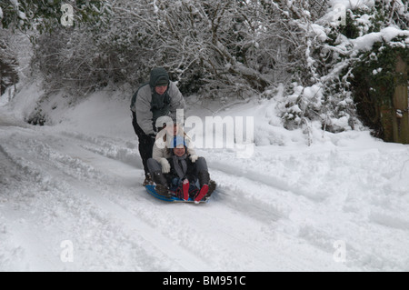 Famille père mère fils garçon sur luge luge dans la neige sur la route enneigée hiver Sussex. Banque D'Images