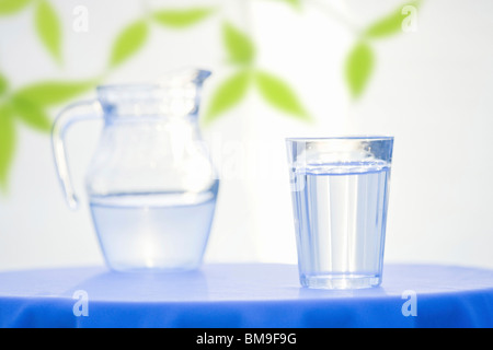 Pichet en verre et avec de l'eau sur la table, fond blanc Banque D'Images