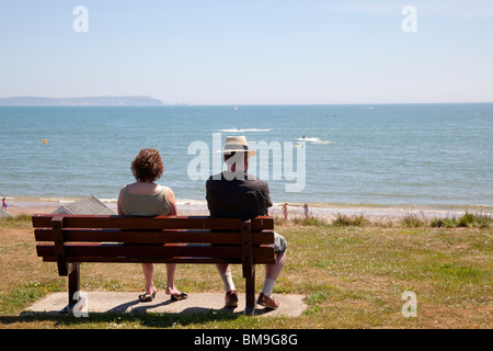 Couple assis sur banc avec vue sur Mudeford plage et la baie sous le soleil d'été Banque D'Images