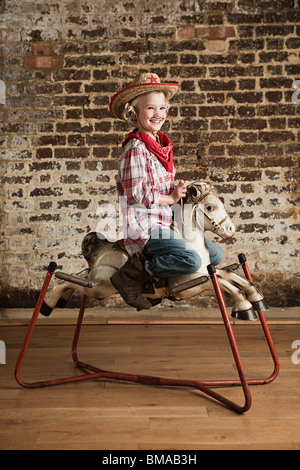 Jeune Fille habillée en cowgirl avec cheval à bascule Banque D'Images
