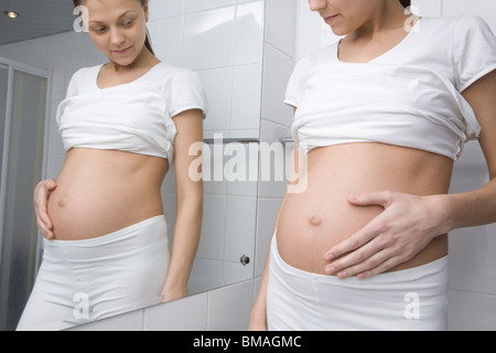 Femme enceinte se tient à l'estomac en miroir de salle à Banque D'Images