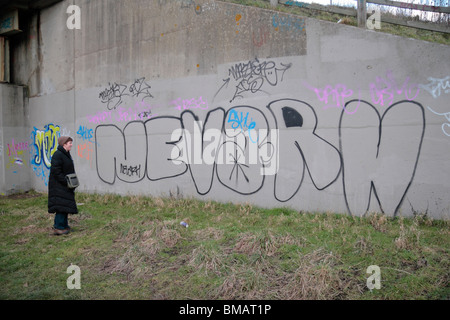 Une femme regarde l'écriture graffiti gribouillé sur un mur en béton à Brentford, Middx, UK. Banque D'Images