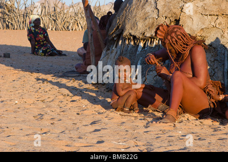 Tribu Himba nomades, la mère et l'enfant zigzag dans chaude soirée du soleil par de la bouse de vache hut habillé en costume traditionnel et argile rouge style de cheveux Banque D'Images