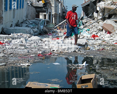 Un homme en compte dans une flaque d'eau pendant qu'il marche à travers les décombres et déchets à Port-au-Prince après le séisme en Haïti Banque D'Images