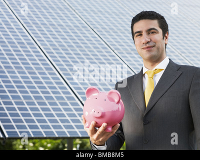 Engineer holding piggy bank et debout près de la station d'énergie solaire Banque D'Images