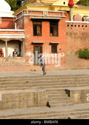 Vieux homme népalais à marcher le long de la vue surplombant les ghats de crémation au temple hindou de Pashupatinath, Katmandou, Népal Banque D'Images