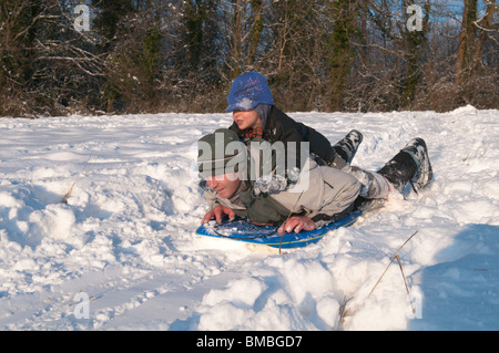 Père et fils de quatre ans boy sitting on sled in snow Banque D'Images