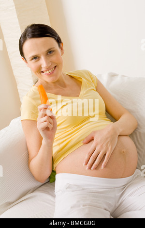 Jeune femme enceinte à la maison manger des carottes Banque D'Images