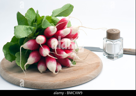 Petit-déjeuner français sur un radis Planche à découper en bois, avec un pot de sel et de couteau, sur un fond blanc. Banque D'Images