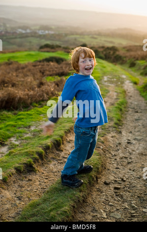 Jeune garçon rire et jouer en marchant au coucher du soleil dans la campagne. Banque D'Images