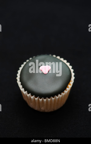 Mini cupcake décoré de glaçage noir et un coeur de sucre sur un fond noir Banque D'Images