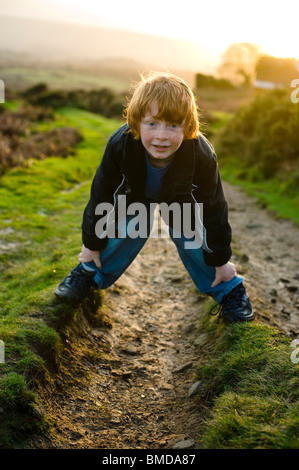 Jeune garçon rire et jouer en marchant au coucher du soleil dans la campagne. Banque D'Images