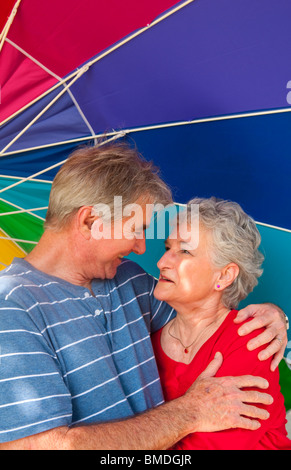 La retraite en bonne santé senior couple smiling ihappy sous parapluie coloré à l'extérieur Banque D'Images