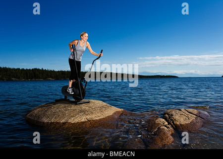 Jeune femme sur un groupe de travail sur une pierre dans un lac, la Suède. Banque D'Images