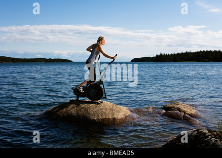 Jeune femme sur un groupe de travail sur une pierre dans un lac, la Suède. Banque D'Images