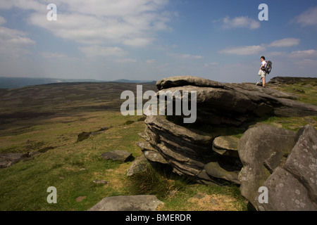 Lone lady walker sur Stanage Edge falaises pierre meulière, parc national de Peak District, Derbyshire. Banque D'Images