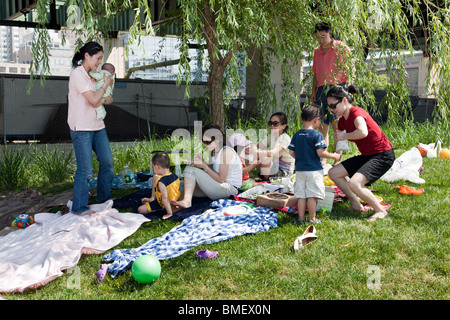 Famille Américaine Chinoise y compris Mère avec enfant profiter de pique-nique sur l'herbe à Riverside Park à proximité de l'autoroute pylône Banque D'Images