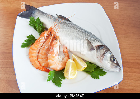 Plaque avec loup de mer, gambas, citron et persil isolé sur fond de bois Banque D'Images