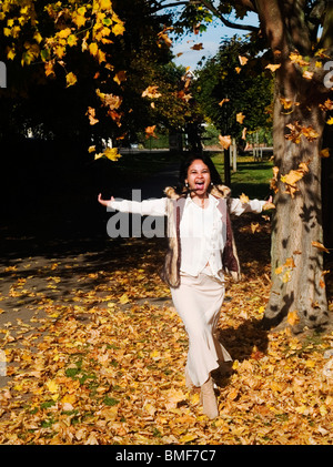 Jeune femme s'amusant dans un tapis de feuilles mortes Banque D'Images