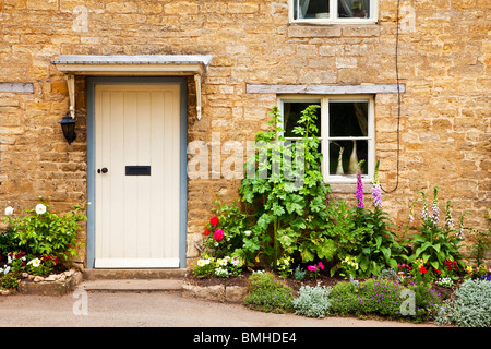 Porte d'un blanc Cotswold typique maison de village en pierre avec un joli gîte jardin avant de fleurs d'été Banque D'Images