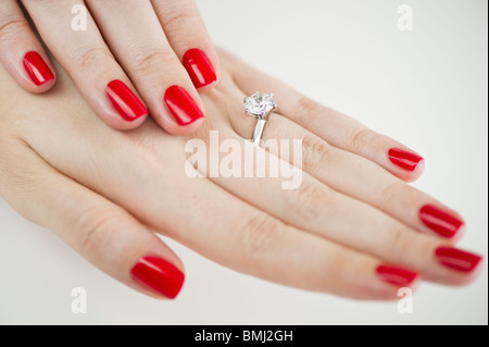 Bague de fiançailles en diamants sur les mains avec le vernis à ongles rouge Banque D'Images