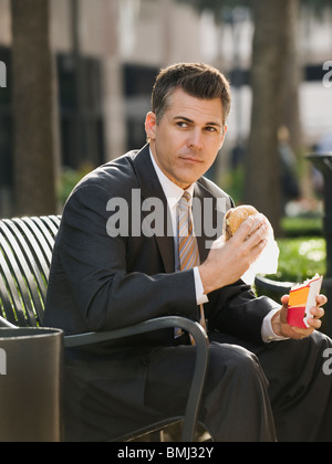 Businessman eating lunch sur banc de parc Banque D'Images