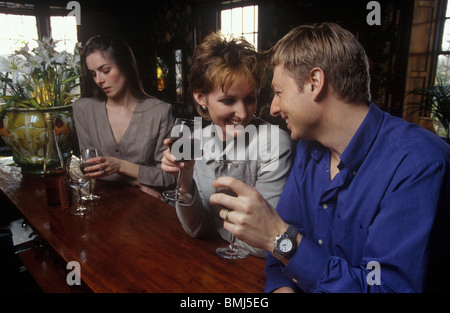 Un couple ayant un verre ensemble dans un bar avec une femme dans l'arrière-plan à la marre Banque D'Images