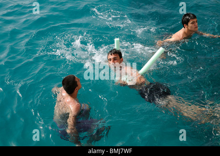 Jeune homme à l'aide d'une piscine et nouilles comme une aide à la flottabilité il flotte dans la mer avec des amis Banque D'Images