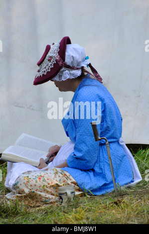 Femme vêtue de vêtements historiques (Révolution Américaine Guerre froide) livre de lecture au camp de l'armée tente Banque D'Images