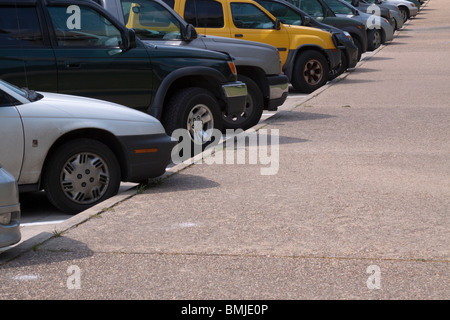 Rangée de voitures et de vus en diagonale garé le long d'une bordure avec un SUV jaune vif au milieu. Banque D'Images