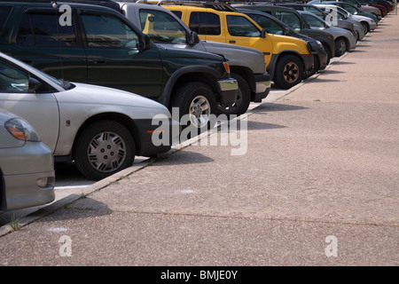 Rangée de voitures et de vus en diagonale garé le long d'une bordure avec un SUV jaune vif au milieu. Banque D'Images