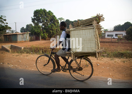 L'Afrique de l'ouest, au Bénin. L'homme fait son chemin vers le bas road transport de lourdes charge sur vélo. Banque D'Images