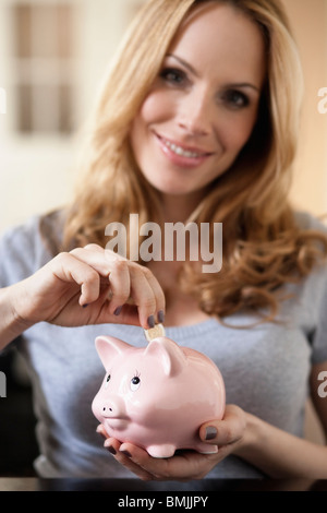 Woman putting coins in piggy bank à Banque D'Images