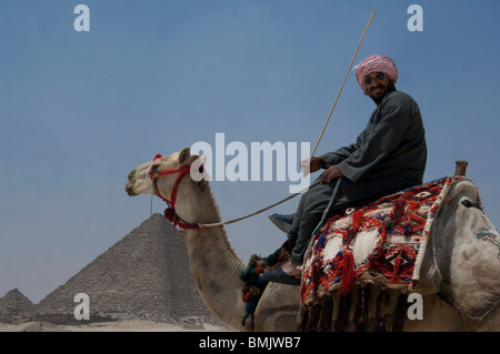 L'Egypte, Le Caire. L'Homme égyptien en tenue traditionnelle en face de chameau sur les grandes pyramides de Gizeh. Banque D'Images