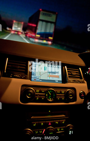 L'intérieur du Range Rover voiture montrant sat nav et compose sur planche de bord la nuit sur l'autoroute à la circulation. UK Banque D'Images