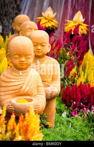 Quatre figures d'Asie en terre cuite dans un jardin de fleurs colorées Banque D'Images