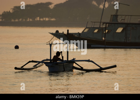 Un jeune garçon balinais paddles out au lever du soleil dans une pêche traditionnelle outrigger appelé un jukung dans le village de Pemuteran. Banque D'Images