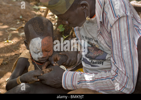 L'Éthiopie, région de l'Omo, Kibish village. Le père dépose de petits éclats fils pied. Banque D'Images