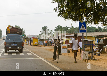 L'Afrique, Afrique de l'Ouest, le Ghana, route côtière. L'homme sur location et de l'homme marchant le long de rue à côté des magasins de plein air. Banque D'Images