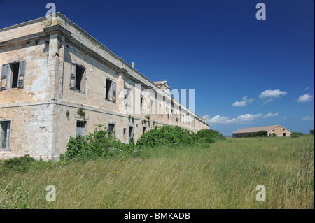 Les bâtiments de l'hôpital militaire à l'abandon, de la Mola, Mahon, Minorque. Pierre de couleur crème est définie sur un ciel bleu profond et vert herbe est au premier plan Banque D'Images