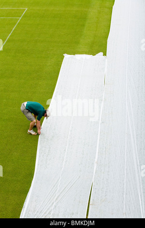 Groundsman à tous les Tennis Club de Wimbledon en Angleterre, SW19, l'application de feuilles de plastique pour une pelouse ensemencée de tennis. UK. Banque D'Images