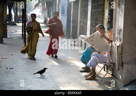 Les hommes la lecture des nouvelles du papier dans la lumière du matin et deux balades femme Bengali, Calcutta Kolkata maintenant, Bengale occidental, Inde Banque D'Images