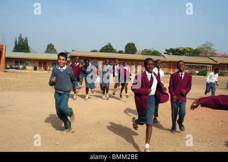 Le Nigéria, Jos, des écoliers et des écolières dans leur uniforme de l'école violet et bleu, courir sur un champ de sable alltogether. Banque D'Images