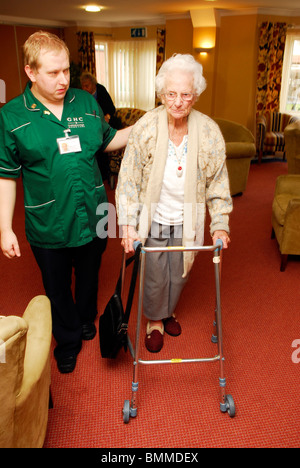 Travailleur de la santé d'aider une personne âgée avec sa mobilité à une maison de retraite, Wirral, UK. Banque D'Images