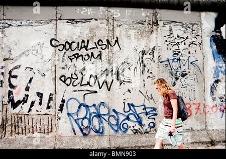 Femme marche passé une section du mur de Berlin, couverts de graffitis Banque D'Images